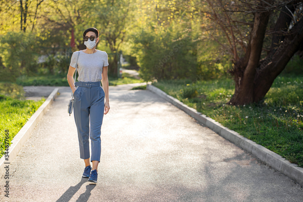 Woman wearing medical mask, alone walks in the park during Covid 19 outbreak. Protection in prevention for coronavirus. Social Distancing concept. Woman wearing medical mask, alone walks in the park during Covid 19 outbreak. Protection in prevention for coronavirus. Social Distancing concept.