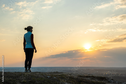 Silhouette of a woman hiker standing alone enjoying sunset outdoors. Female tourist on rural field in evening nature. Tourism  traveling and healthy lifestyle concept.