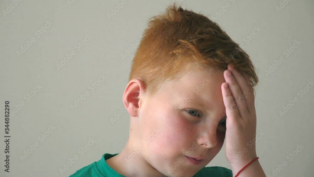 Portrait of serious red hair boy with freckles. Desperate kid thinks about his problems indoor. Close up emotions of male child with sad expression on face. Slow motion Portrait of serious red hair boy with freckles. Desperate kid thinks about his problems indoor. Close up emotions of male child with sad expression on face. Slow motion