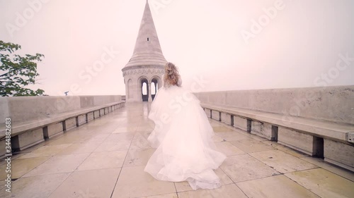 Fashion model, the bride in a chic wedding long dress running walks or walks, from behind and from the outside, looks around. against the background of the architecture of the old town and castle