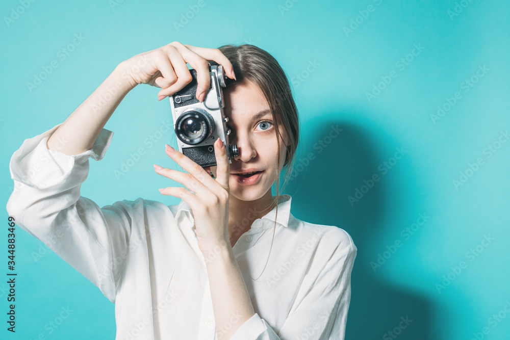 young girl in a white shirt and jeans with a vintage camera on a blue background in the studio young girl in a white shirt and jeans with a vintage camera on a blue background in the studio
