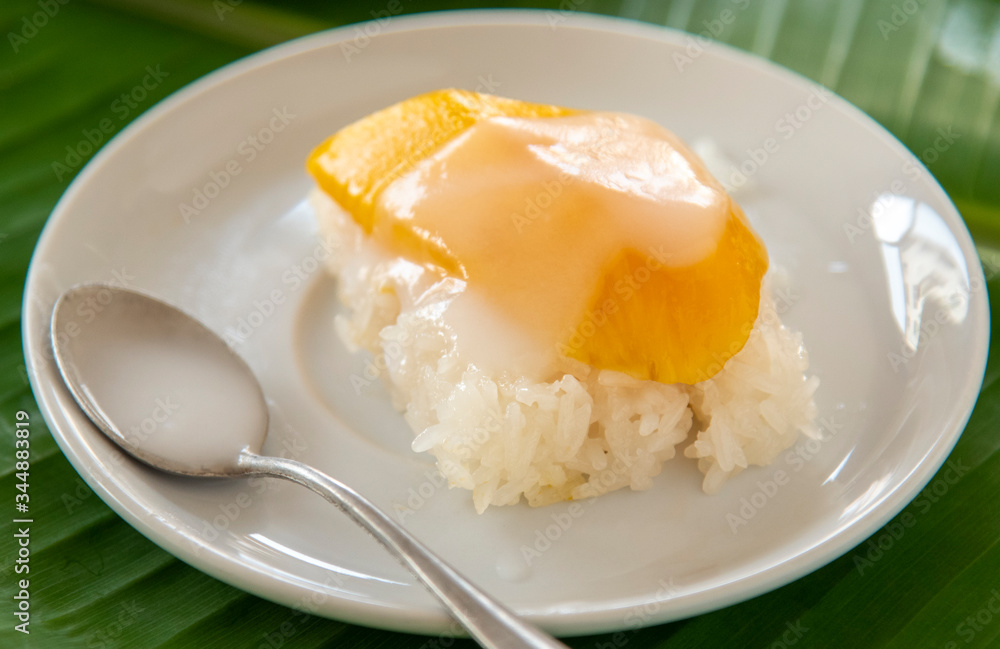 Ripe Mango with sweet sticky rice pour coconut milk in a white dish on a banana leaf. popular Thai dessert. Ripe Mango with sweet sticky rice pour coconut milk in a white dish on a banana leaf. popular Thai dessert.