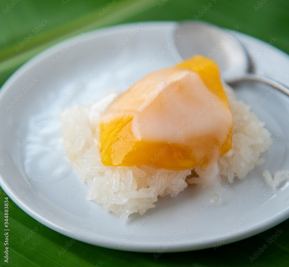 Ripe Mango with sweet sticky rice pour coconut milk in a white dish on a banana leaf. popular Thai dessert. Ripe Mango with sweet sticky rice pour coconut milk in a white dish on a banana leaf. popular Thai dessert.