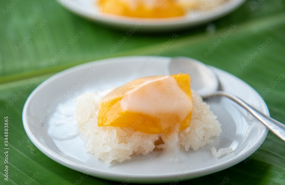 Ripe Mango with sweet sticky rice pour coconut milk in a white dish on a banana leaf. popular Thai dessert. Ripe Mango with sweet sticky rice pour coconut milk in a white dish on a banana leaf. popular Thai dessert.