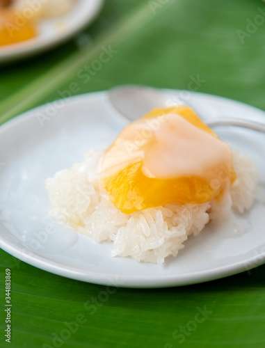 Ripe Mango with sweet sticky rice pour coconut milk in a white dish on a banana leaf. popular Thai dessert.