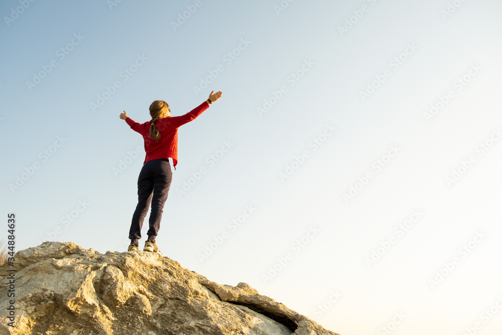 Young woman hiker standing alone on big stone in mountains. Female tourist raising her hands up on high rock in morning nature. Tourism, traveling and healthy lifestyle concept. Young woman hiker standing alone on big stone in mountains. Female tourist raising her hands up on high rock in morning nature. Tourism, traveling and healthy lifestyle concept.