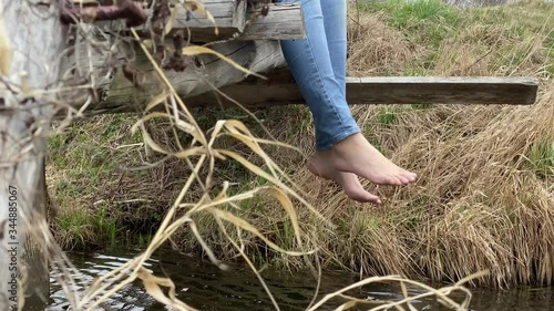 Woman legs in jeans without shoe dangling from old wooden bridge