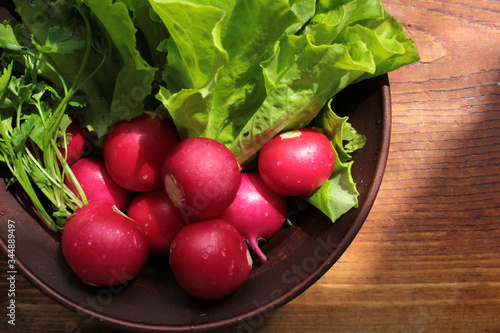 Fresh radish, lettuce and parsley in a brown ceramic salad bowl on a wooden cutboard. Healthy spring food