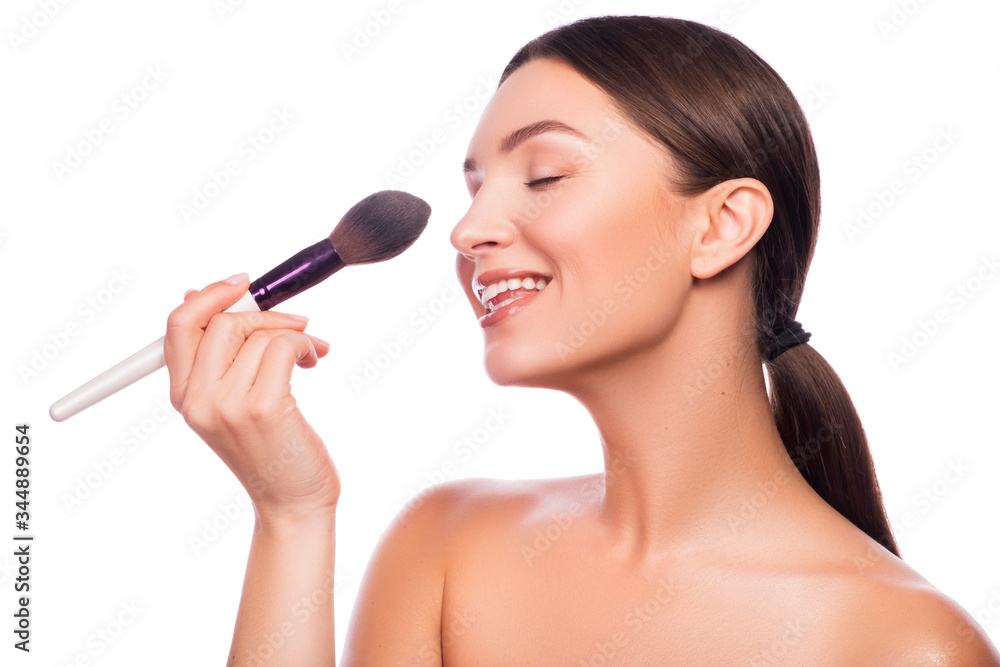Cute smiling brunette adult girl apply make up on her fresh clean face with brush in her hand. Beauty headshot isolated on white. Cute smiling brunette adult girl apply make up on her fresh clean face with brush in her hand. Beauty headshot isolated on white.