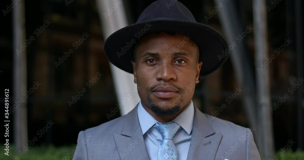 Portrait of stylish guy in hat and suit looking to camera while standing at street. Close up view of handsome african american man in 30s wearing tie posing. Concept of real life. Portrait of stylish guy in hat and suit looking to camera while standing at street. Close up view of handsome african american man in 30s wearing tie posing. Concept of real life.