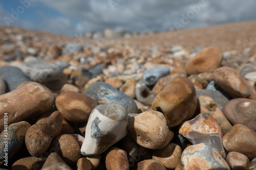 Low angle close focus of pebbles on a beach with blurred shore and buildings in background.Image