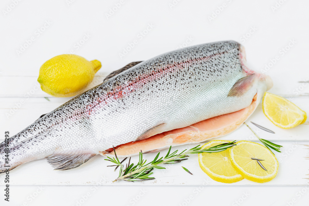 A raw decapitated trout on a white background sliced on one side with a lemon and rosemary leaves next to it. Freshwater fish. A raw decapitated trout on a white background sliced on one side with a lemon and rosemary leaves next to it. Freshwater fish.