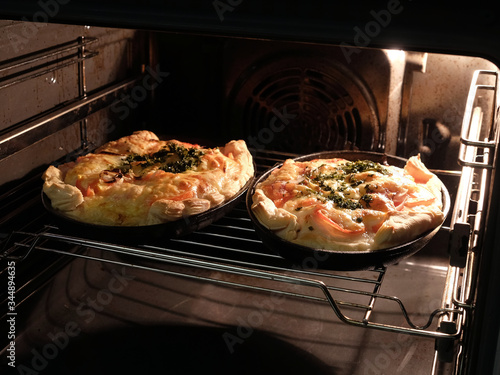 Two big homemade prepared pizza with bacon tomatoes and cheese inside in the kitchen stove front view closeup