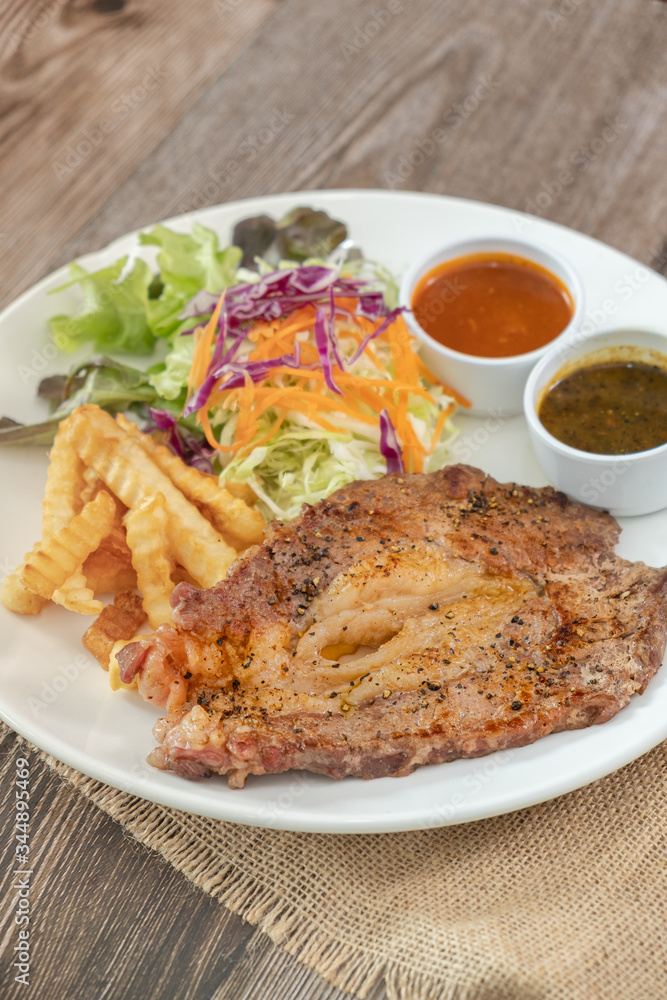 Beef steak with barbecue and paper sauces, side dish salad and french fries served on white plate, wooden table. Beef steak with barbecue and paper sauces, side dish salad and french fries served on white plate, wooden table.