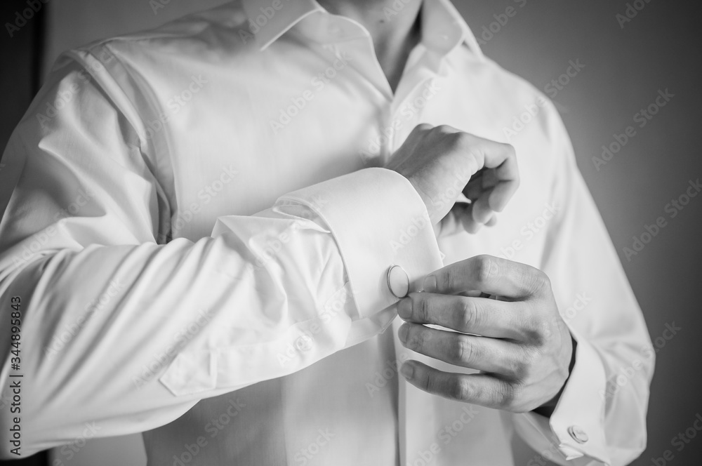 A groom fastening a cuff-link on the shirt