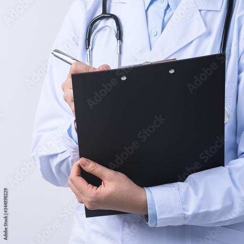 Doctor with stethoscope in white coat holding clipboard, writing medical record diagnosis, isolated on white background, close up, cropped view.