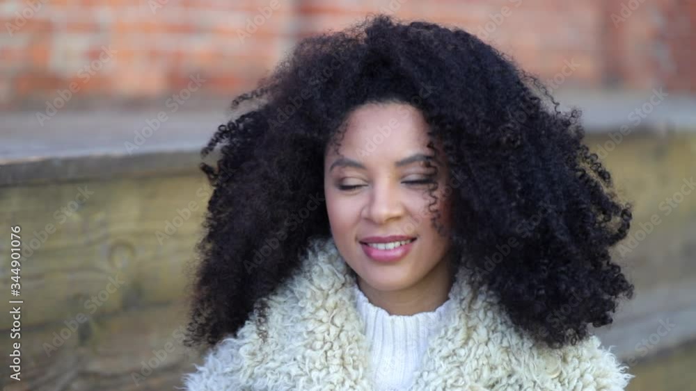 Portrait of beautiful african american woman looking at camera with smile standing outdoors spbi. Young curly female is smiling and posing while having nice day on street. Lady wearing casual clothes
