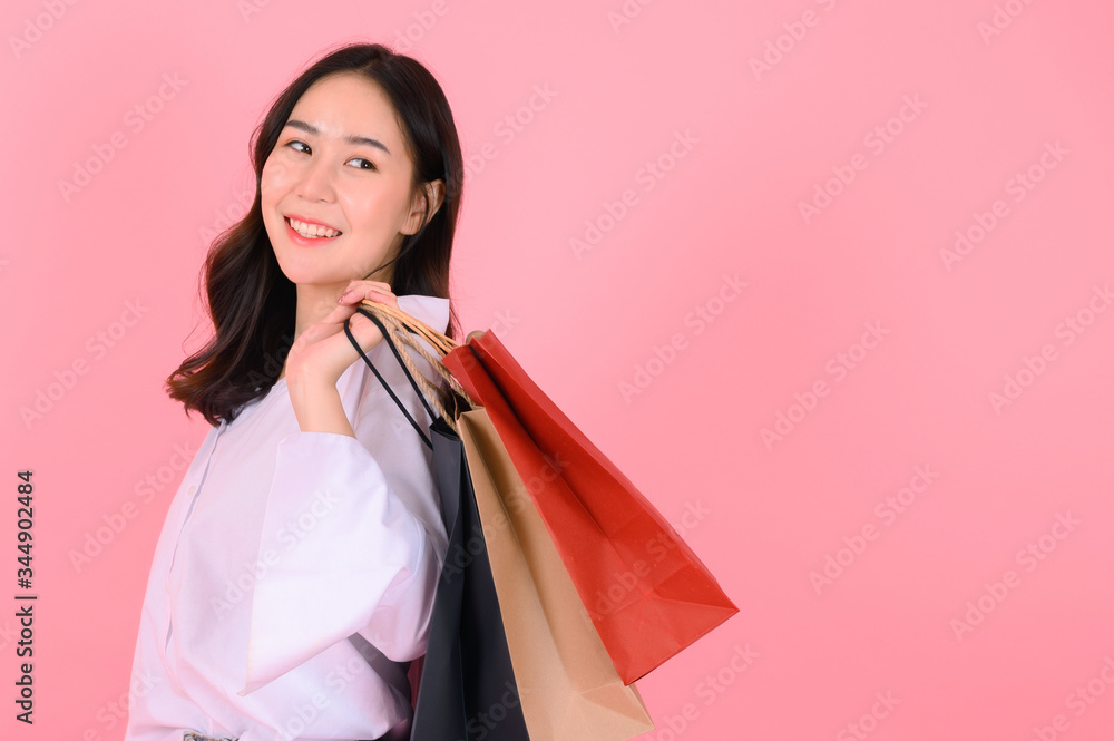 Portrait of beautiful asian girl holding shopping bags isolated on pink background