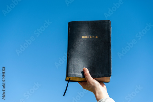 Raised hand holding the Holy Bible. Background with blue sky on a beautiful winter morning. Copy space. Close-up. Horizontal shot.