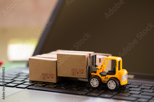 Logistic and cargo freight concept: Fork-lift a truck moves a paper box on notebook keyboard. depicts International freight or shipping service for online shopping.