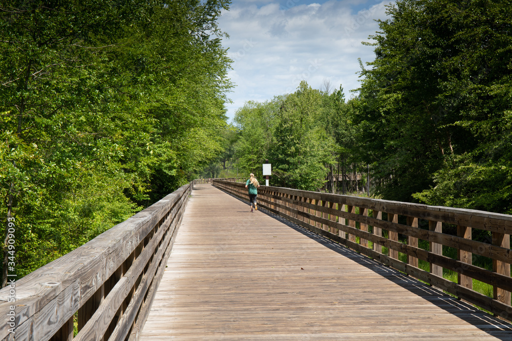 Woman running down a long elevated boardwalk, blank sign for text, horizontal aspect Woman running down a long elevated boardwalk, blank sign for text, horizontal aspect
