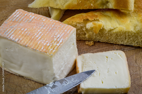 Piece of sliced taleggio italian cheese with focaccia bread on a wooden cutting board with knife close up.