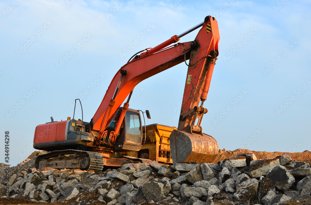 Excavator with a large iron bucket breaks asphalt on a construction site. Demolition work concrete, replacing asphalt, road works. Mobile Stone crusher machine at backhoe crawler Excavator with a large iron bucket breaks asphalt on a construction site. Demolition work concrete, replacing asphalt, road works. Mobile Stone crusher machine at backhoe crawler
