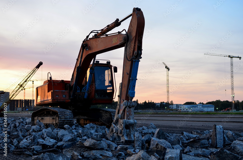 Excavator with hydraulic shears at construction site against the background sunset. Road repair, Demolition work concrete, replacing asphalt Excavator with hydraulic shears at construction site against the background sunset. Road repair, Demolition work concrete, replacing asphalt