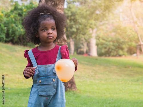 Cute adorable African girl holding orange heart shape balloon in the hand.