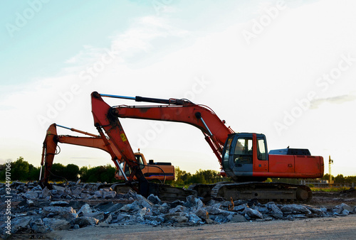 Crawler excavator with hydraulic breaker hammer on sunset. Destruction, demolition of concrete and hard rock at the construction site or quarry. Jackhammer using without blasting method