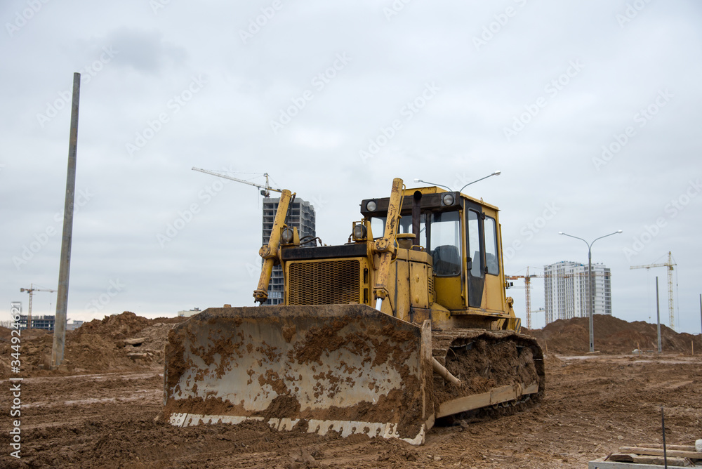 Bulldozer during land clearing and foundation digging at large construction site. Crawler tractor with bucket for pool excavation and utility trenching. Dozer, Earth-moving equipment Bulldozer during land clearing and foundation digging at large construction site. Crawler tractor with bucket for pool excavation and utility trenching. Dozer, Earth-moving equipment