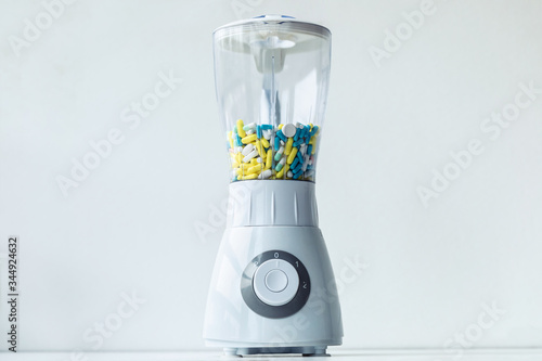 A white blender with multicolored capsules and pills. Nutritional supplementation concept.