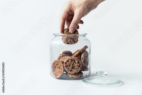Photography A hand taking cookies from a glass jar on white background.