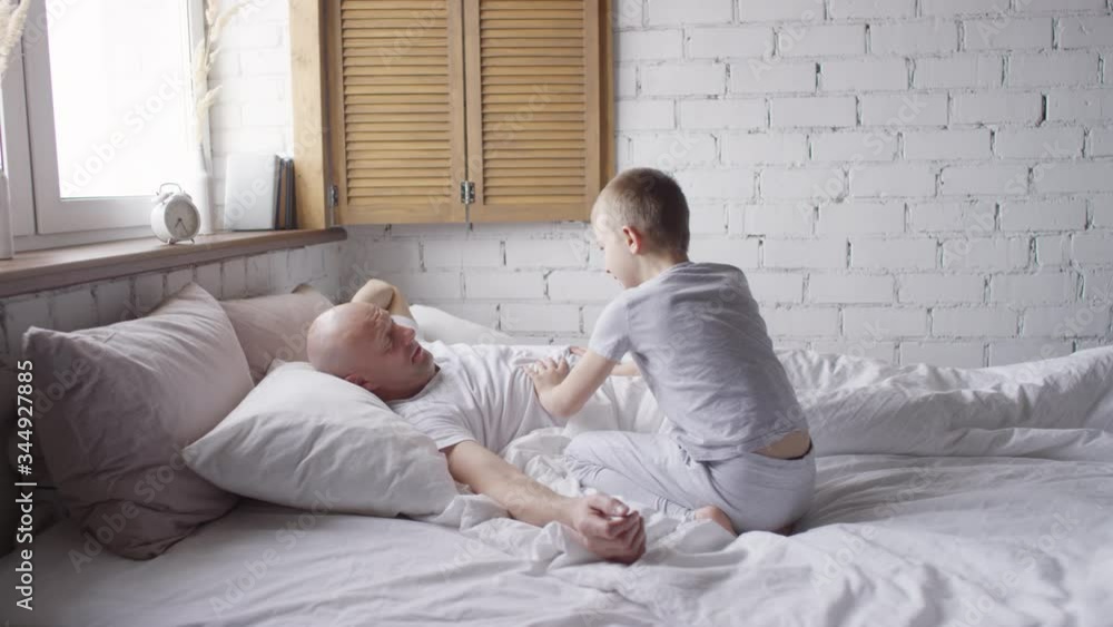 Slowmo shot of playful schoolboy in sleepwear running into his fathers bedroom and waking him up Slowmo shot of playful schoolboy in sleepwear running into his fathers bedroom and waking him up