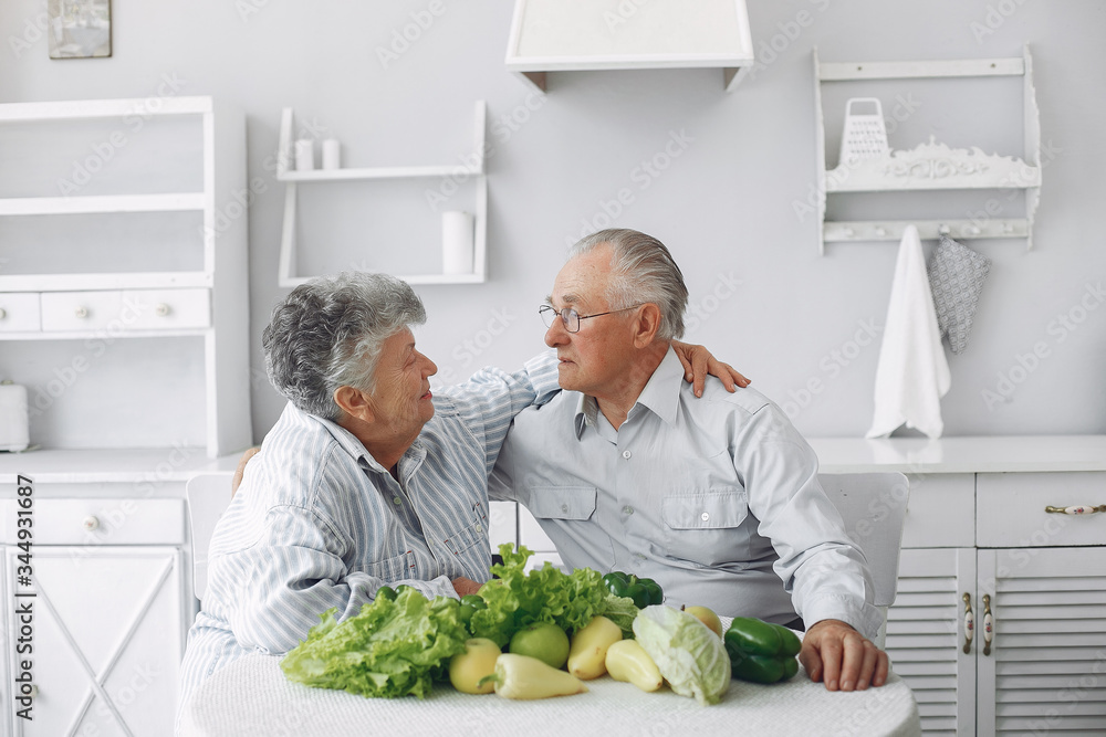 Couple in a kitchen. Grandparents sitting at home. Woman with vegetables Couple in a kitchen. Grandparents sitting at home. Woman with vegetables