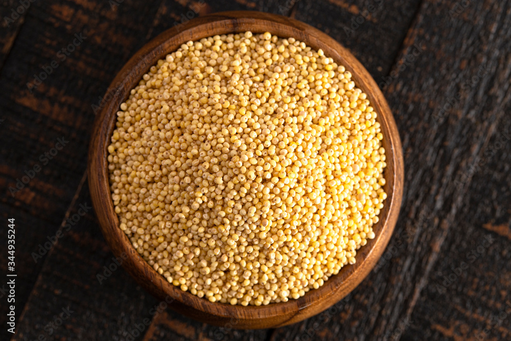Bowl of Whole Millet in a Wood Bowl on a Rustic Dark Wood Table Bowl of Whole Millet in a Wood Bowl on a Rustic Dark Wood Table