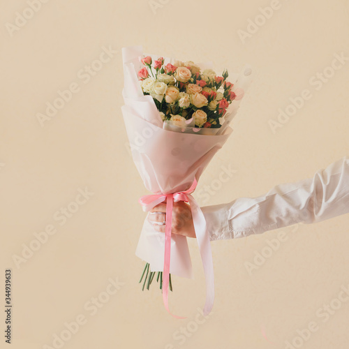 Hand in white shirt with roses bouquet close up on beige background. Soft tender colors. 