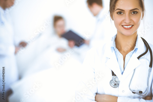 Female doctor smiling on the background with patient in the bed and two doctors photo