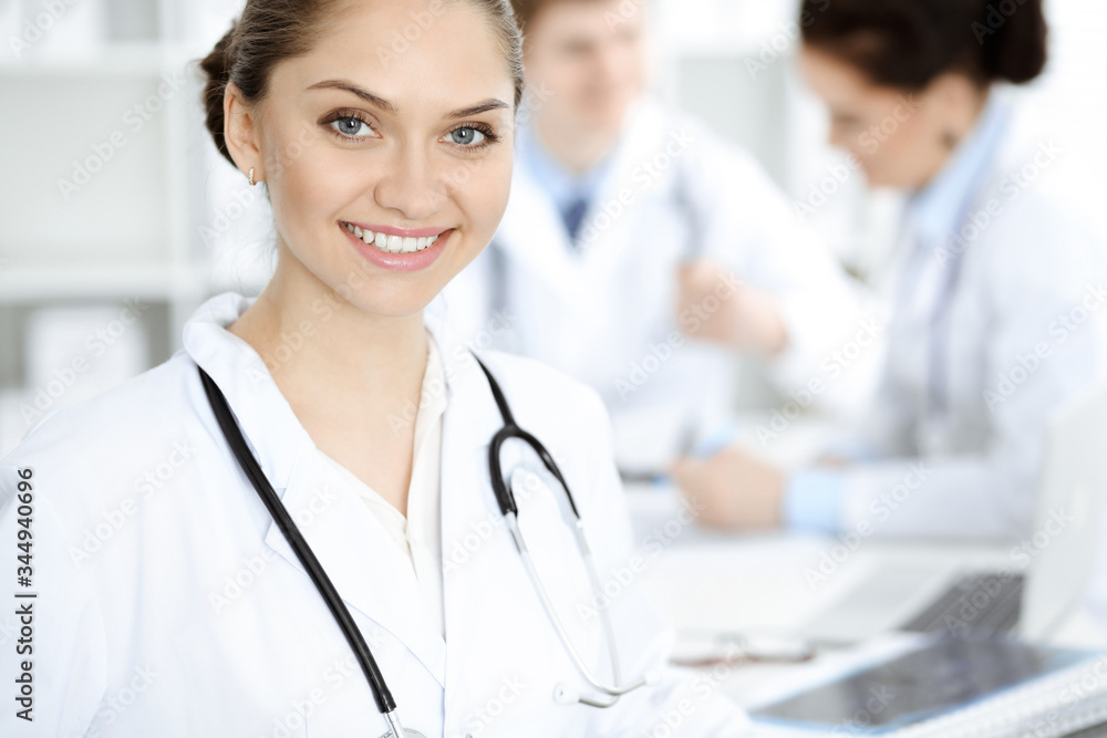 Happy smiling woman-doctor sitting and looking at camera at meeting with medical staff . Medicine concept