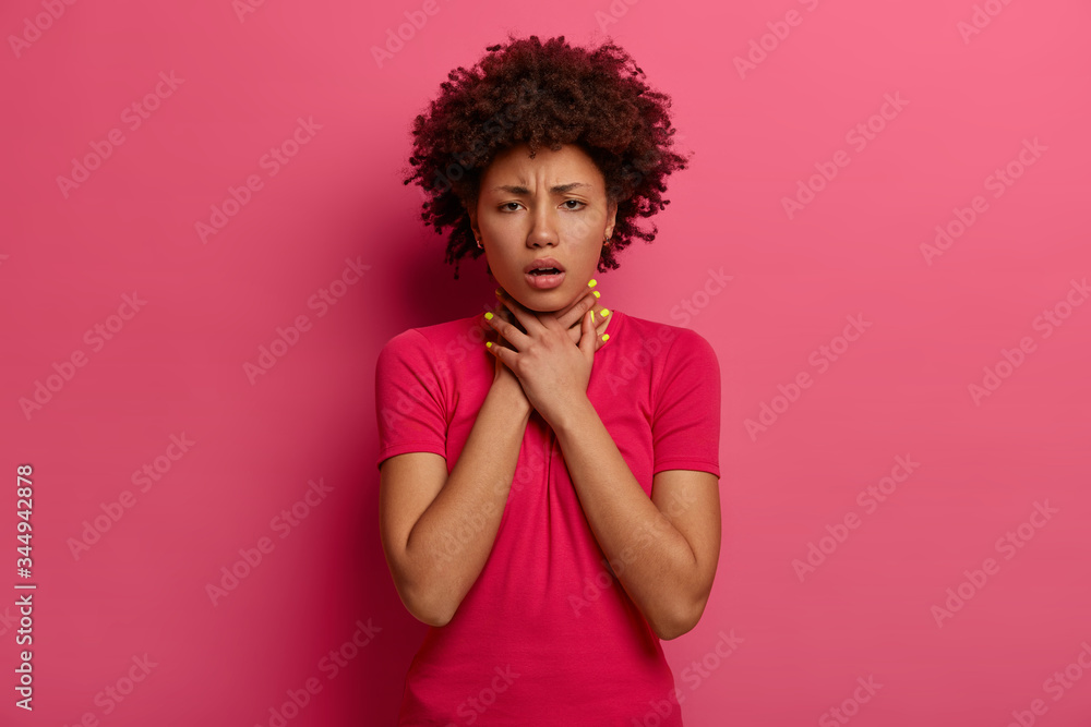 Displeased dark skinned woman has asthma attack, cannot breath well, keeps hands on neck, frowns face, suffocates or chokes, coughs, has problems with health, wears casual clothes, isolated on pink Displeased dark skinned woman has asthma attack, cannot breath well, keeps hands on neck, frowns face, suffocates or chokes, coughs, has problems with health, wears casual clothes, isolated on pink