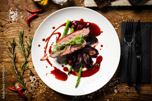 Duck breast with asparagus, salad and sauce on white plate. Delicious healthy grilled and roasted bird fillet food closeup served on a table for lunch in modern cuisine gourmet restaurant. photo