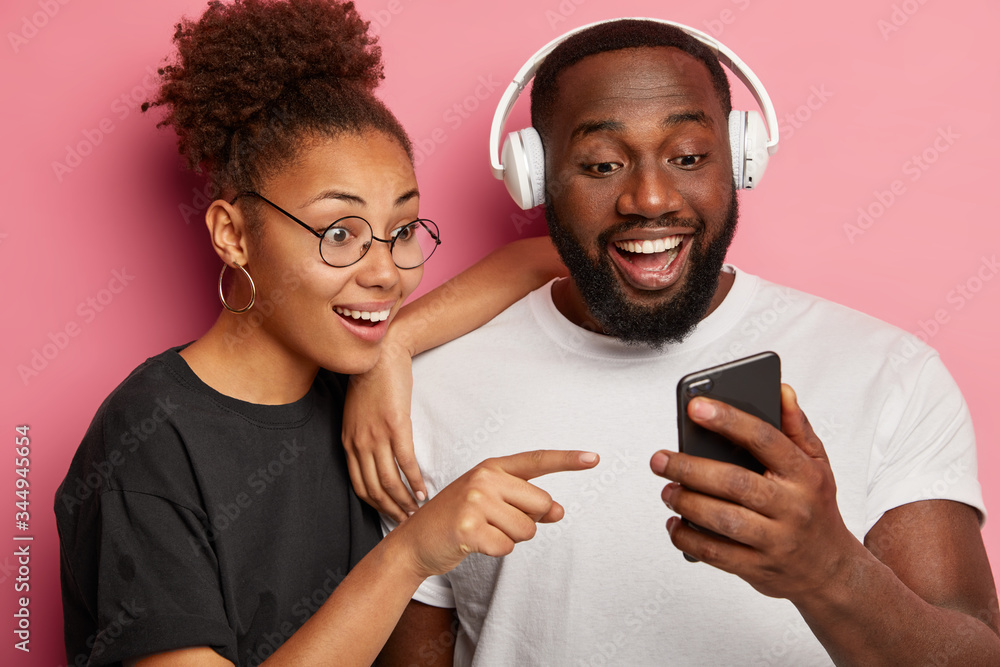 Happy ethnic girlfriend boyfriend look cheerfully at smartphone