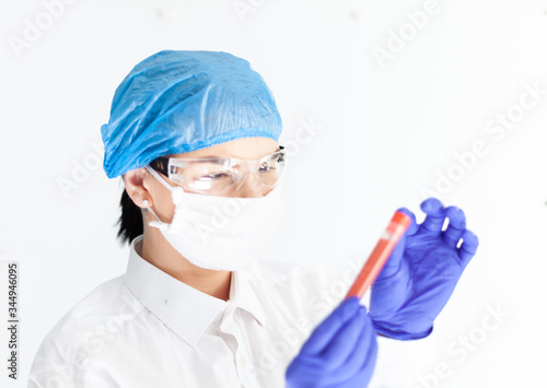 female doctor in safety glasses  mask and gloves looks at a test tube with blood