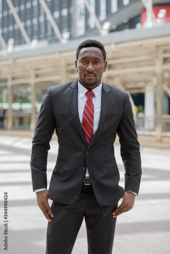 Young handsome African businessman standing in front of modern building at Bangkok city Young handsome African businessman standing in front of modern building at Bangkok city
