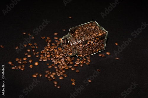 Quadro em tela a glass jar of coffee beans lies on its side against a black background