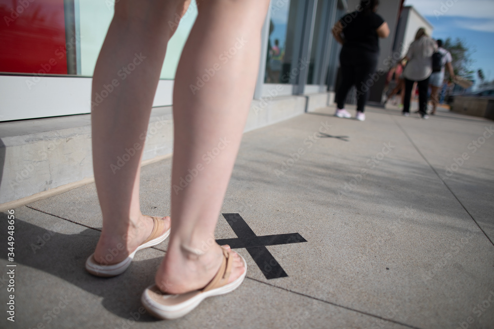 People standing in line far from each other to maintain a distance during the outbreak of the coronavirus COVID-19 with marks on the cross on the sidewalk in front of the department store doors People standing in line far from each other to maintain a distance during the outbreak of the coronavirus COVID-19 with marks on the cross on the sidewalk in front of the department store doors