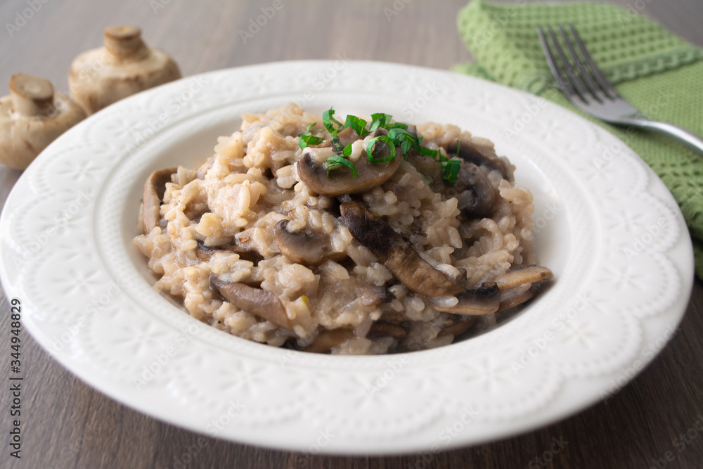 Classic Italian vegan mushroom risotto made with arborio rice, mushrooms, onion and garlic garnished with basil ribbons on a rustic wooden surface with a green napkin and a fork Classic Italian vegan mushroom risotto made with arborio rice, mushrooms, onion and garlic garnished with basil ribbons on a rustic wooden surface with a green napkin and a fork