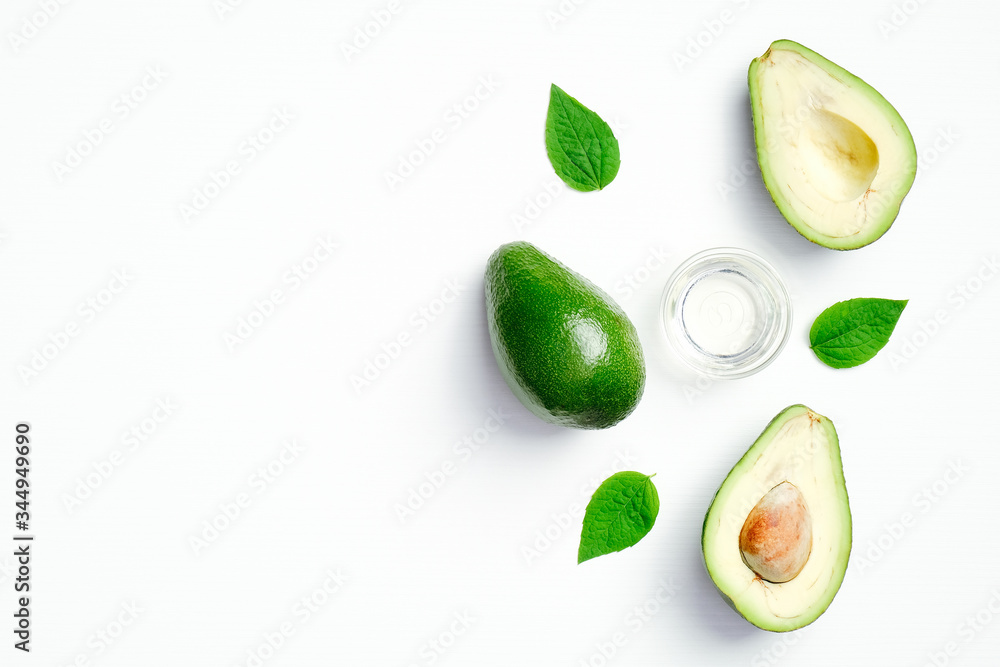 Flat lay fresh avocado and bowl of essential oil with green leaves on white background. Top view natural avocado beauty product, skin care and body treatment concept Flat lay fresh avocado and bowl of essential oil with green leaves on white background. Top view natural avocado beauty product, skin care and body treatment concept