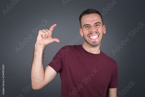 Blond European man over isolated background gesturing with hand showing small size, measure symbol. Smiling looking at the camera. Measuring concept.