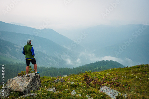A man stands on a hill in front of a foggy mountain valley. Foggy weather high in the mountains in summer